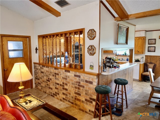 bar featuring a textured ceiling, brick wall, beamed ceiling, and light tile patterned floors