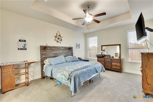 bedroom featuring light carpet, ceiling fan, a raised ceiling, and baseboards