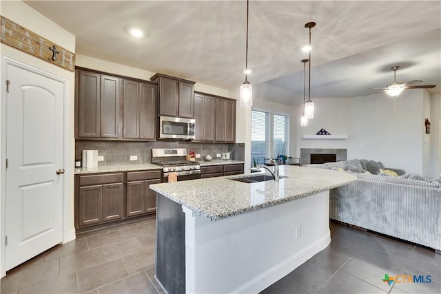 kitchen with light stone counters, a sink, open floor plan, appliances with stainless steel finishes, and backsplash