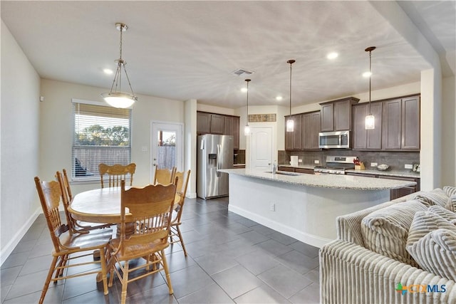 kitchen featuring baseboards, decorative backsplash, a kitchen island with sink, stainless steel appliances, and a sink