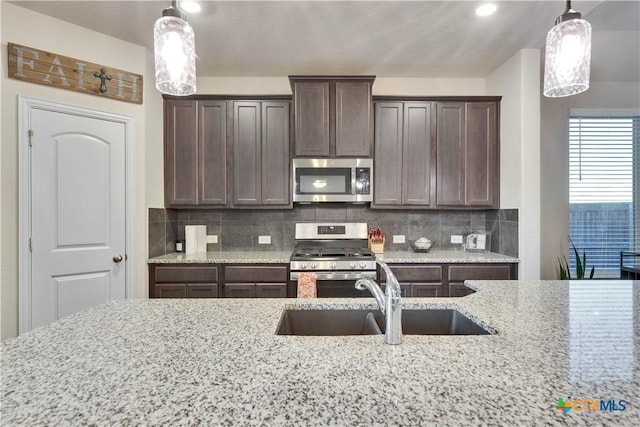 kitchen featuring pendant lighting, backsplash, appliances with stainless steel finishes, a sink, and dark brown cabinetry