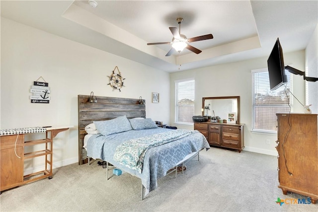 bedroom featuring light carpet, a raised ceiling, and baseboards