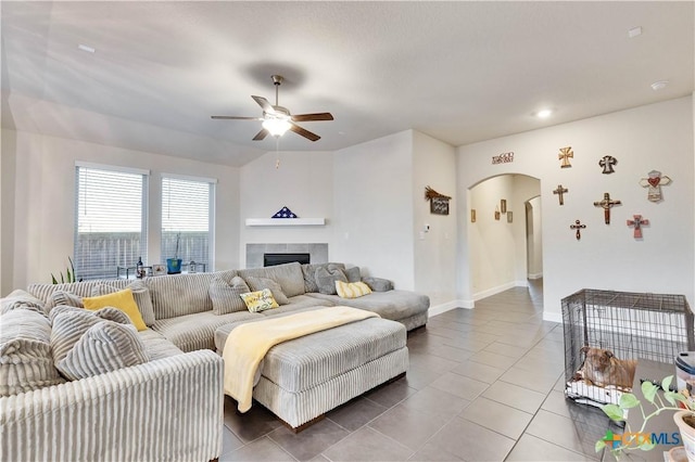 tiled living area with ceiling fan, arched walkways, baseboards, and a tile fireplace