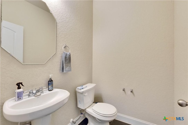 half bathroom with a textured wall, a sink, toilet, and baseboards