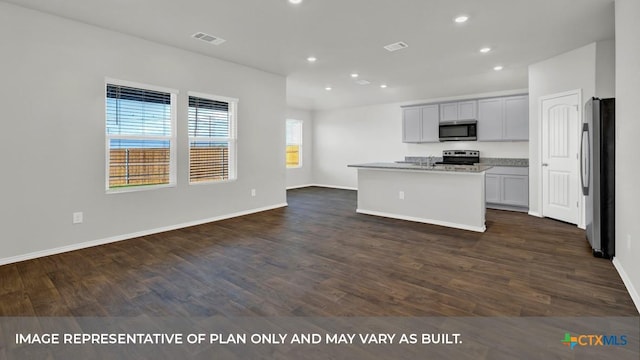 kitchen featuring dark hardwood / wood-style flooring, light stone countertops, an island with sink, and appliances with stainless steel finishes