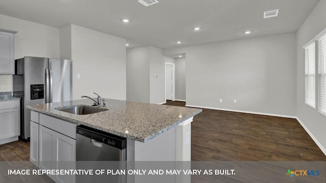 kitchen with light stone countertops, stainless steel appliances, dark wood-type flooring, sink, and a center island with sink