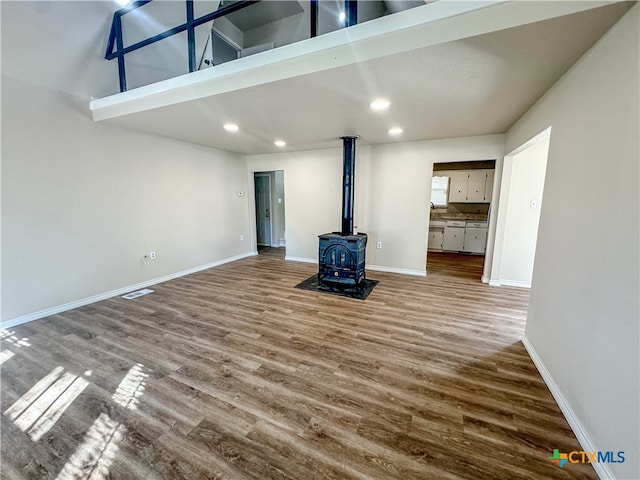 unfurnished living room with a towering ceiling, wood-type flooring, and a wood stove