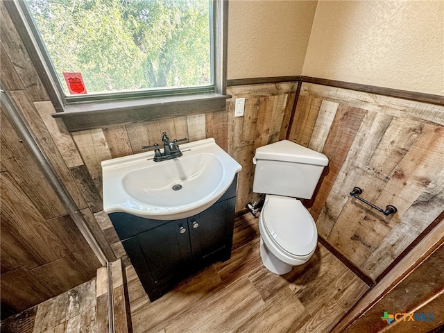 bathroom featuring wood walls, wood-type flooring, toilet, and vanity