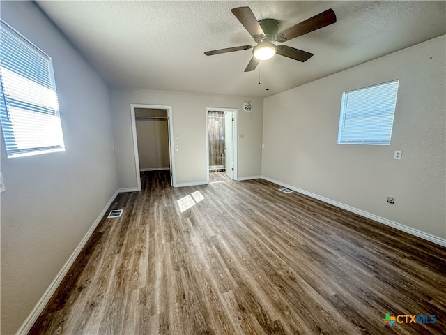 unfurnished bedroom with a walk in closet, wood-type flooring, ceiling fan, and a textured ceiling