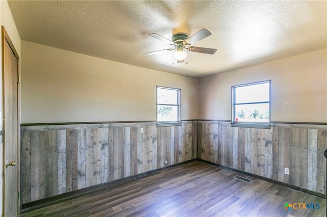 spare room featuring dark hardwood / wood-style flooring, wood walls, a textured ceiling, and ceiling fan