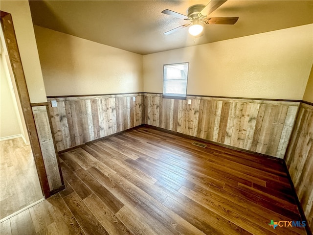 unfurnished room featuring dark hardwood / wood-style flooring, wood walls, and ceiling fan