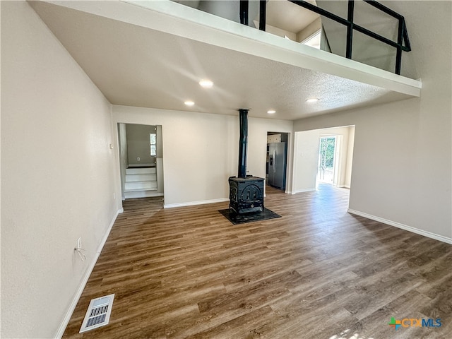 unfurnished living room with wood-type flooring, a textured ceiling, and a wood stove