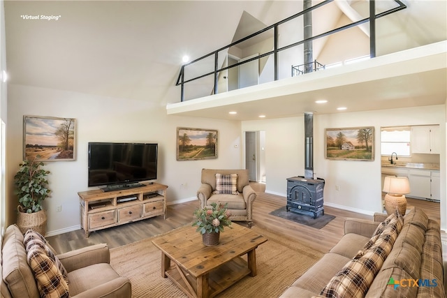 living room with sink, a wood stove, high vaulted ceiling, and light hardwood / wood-style flooring