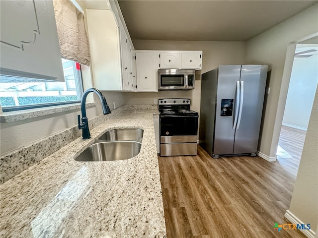 kitchen featuring white cabinetry, sink, light stone counters, appliances with stainless steel finishes, and light wood-type flooring