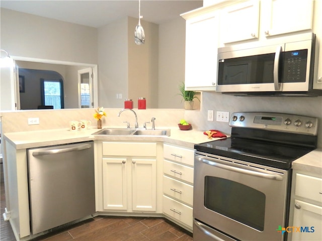 kitchen featuring kitchen peninsula, appliances with stainless steel finishes, dark wood-type flooring, sink, and hanging light fixtures