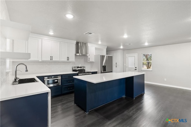 kitchen featuring appliances with stainless steel finishes, wall chimney exhaust hood, sink, a center island, and white cabinetry