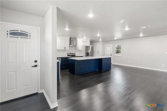 kitchen featuring stainless steel appliances, dark wood-type flooring, wall chimney range hood, white cabinets, and a kitchen island