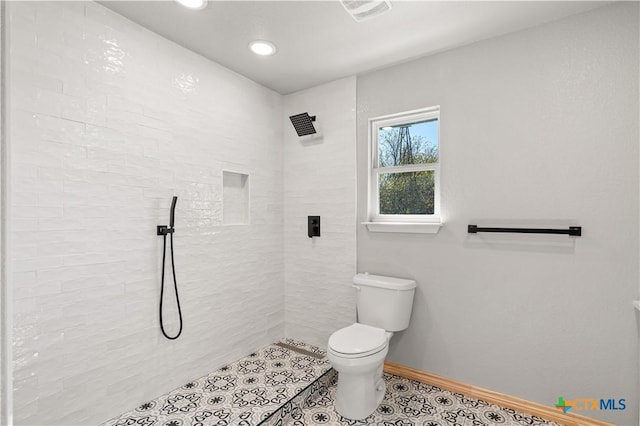 bathroom featuring tile patterned flooring, a tile shower, and toilet