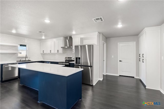 kitchen with stainless steel appliances, sink, wall chimney range hood, white cabinetry, and a kitchen island