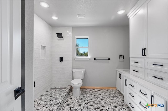 bathroom featuring a tile shower, vanity, and toilet