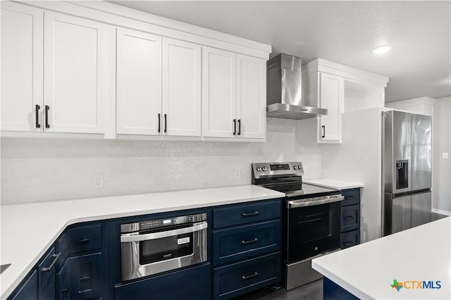 kitchen with blue cabinetry, appliances with stainless steel finishes, white cabinetry, and wall chimney range hood