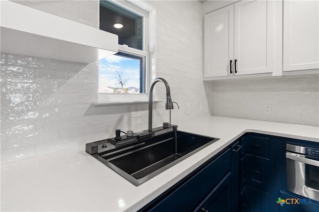 kitchen featuring tasteful backsplash, white cabinetry, sink, and stainless steel oven