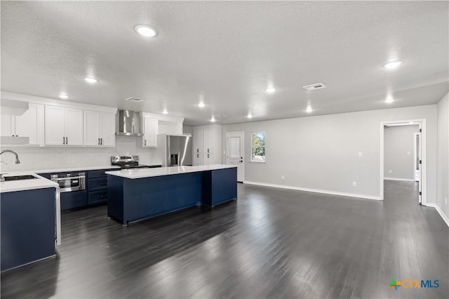 kitchen with a center island, sink, wall chimney exhaust hood, appliances with stainless steel finishes, and white cabinetry