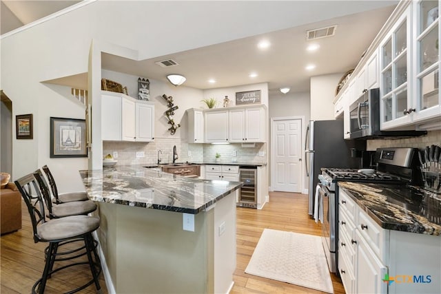 260 County Road 413, Spicewood, TX 78669 - kitchen with stainless steel appliances, a peninsula, wine cooler, a kitchen bar, and light wood-style floors