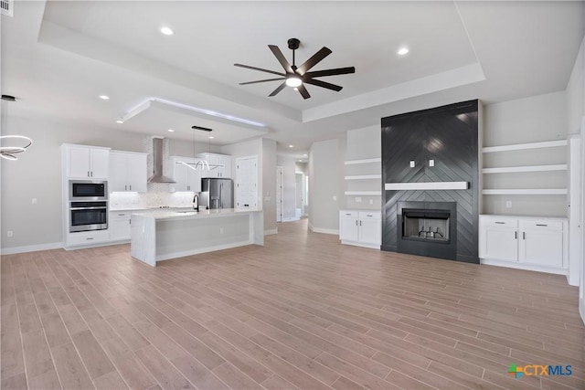 20029 Continental Dr, Lago Vista, TX 78645 - unfurnished living room with a ceiling fan, a tray ceiling, a sink, baseboards, and light wood-type flooring