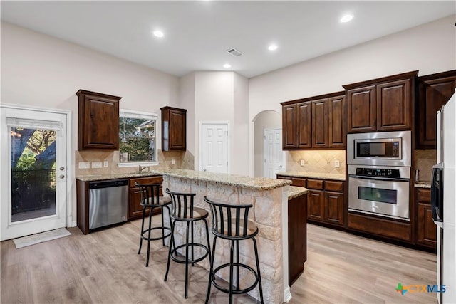 kitchen featuring a center island, a kitchen breakfast bar, light stone counters, appliances with stainless steel finishes, and light wood-type flooring