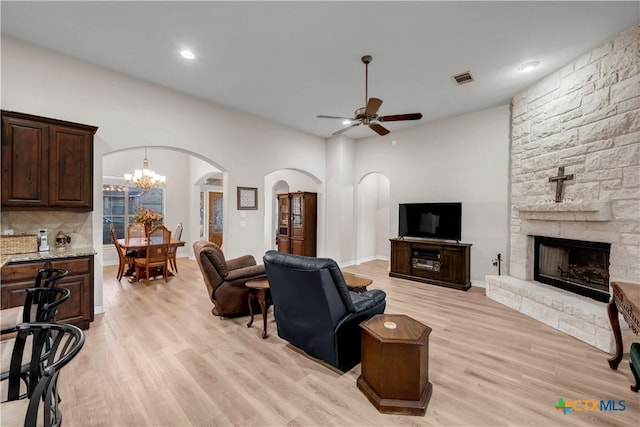 living room featuring ceiling fan with notable chandelier, a stone fireplace, and light wood-type flooring