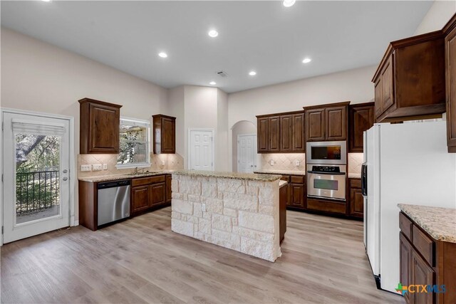 kitchen featuring stainless steel appliances, tasteful backsplash, a breakfast bar, dark brown cabinets, and light wood-type flooring