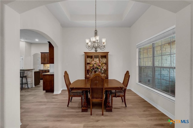 dining space featuring a tray ceiling, light wood-type flooring, and an inviting chandelier