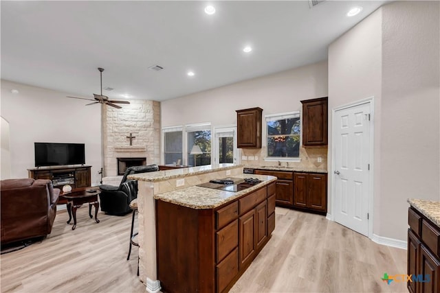 kitchen featuring a center island, a stone fireplace, light hardwood / wood-style floors, a kitchen bar, and black electric cooktop