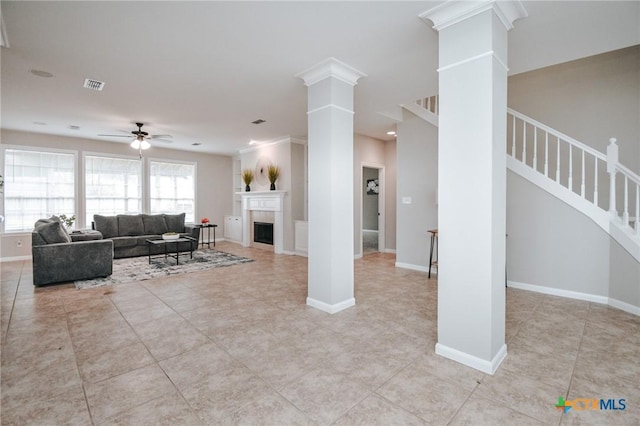 living area featuring visible vents, decorative columns, ceiling fan, and stairway
