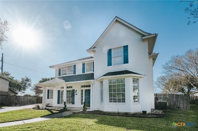 traditional-style home with central AC, fence, and a front lawn