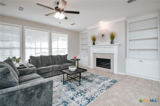 living room with visible vents, a ceiling fan, built in shelves, and a tile fireplace