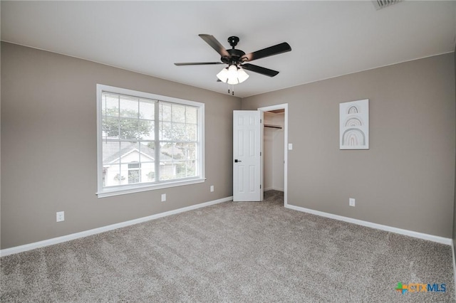 unfurnished bedroom with a walk in closet, carpet floors, a ceiling fan, baseboards, and visible vents