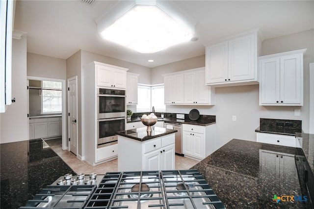 kitchen featuring white cabinets, stainless steel appliances, dark stone countertops, and a center island