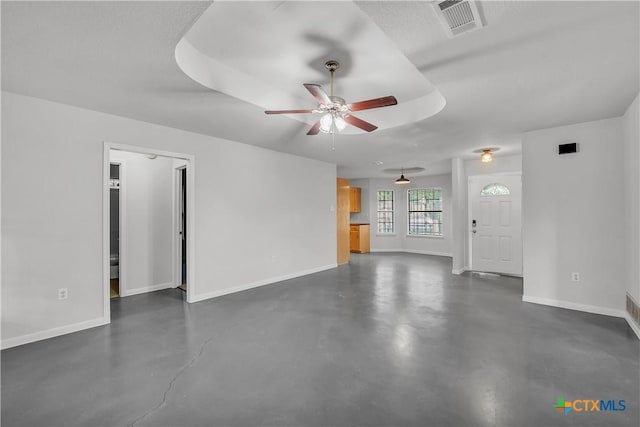 unfurnished living room featuring baseboards, concrete flooring, ceiling fan, and a raised ceiling