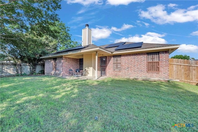 back of property featuring brick siding, a chimney, and solar panels