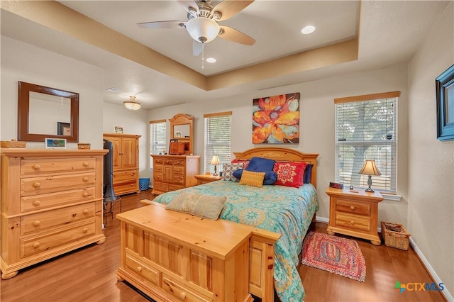 bedroom featuring a tray ceiling, multiple windows, wood finished floors, and baseboards