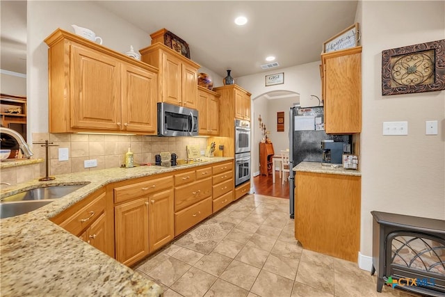 kitchen featuring arched walkways, a sink, light stone countertops, stainless steel appliances, and backsplash