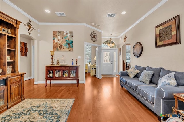 living area featuring visible vents, arched walkways, baseboards, light wood-style flooring, and ornamental molding