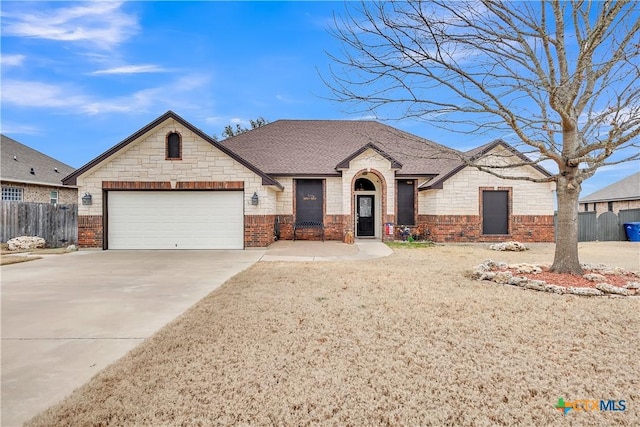 view of front facade featuring brick siding, roof with shingles, fence, a garage, and driveway