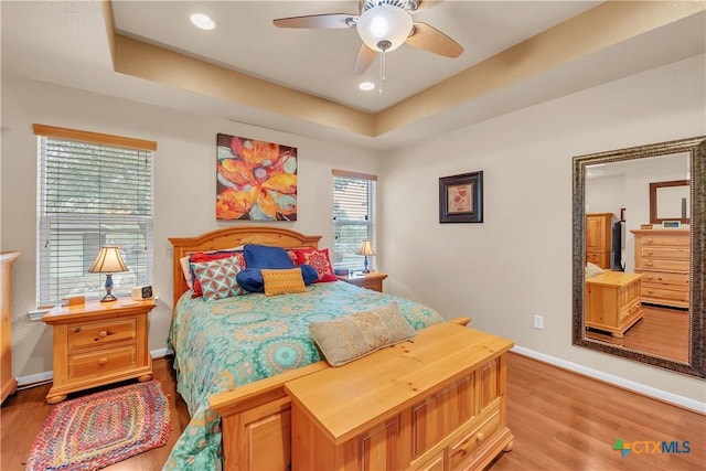 bedroom with ceiling fan, recessed lighting, baseboards, light wood-type flooring, and a tray ceiling