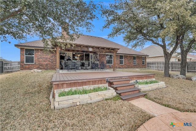 back of property featuring brick siding, a fenced backyard, a yard, and a wooden deck