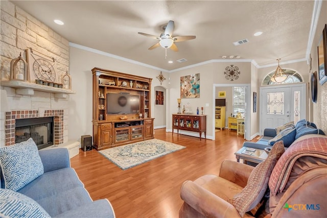 living area featuring a large fireplace, light wood-style flooring, visible vents, and crown molding