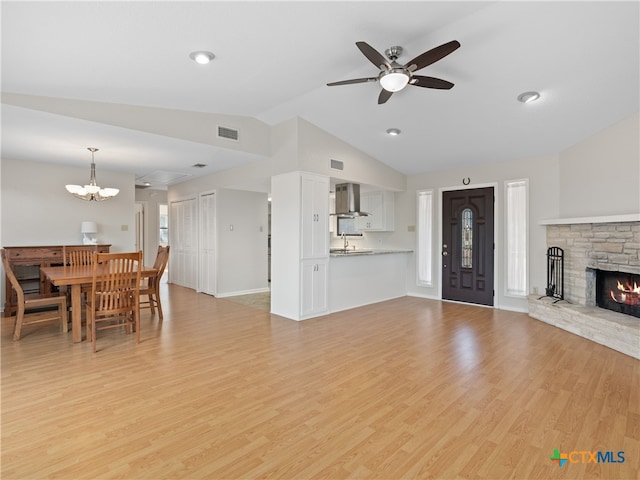 living room with lofted ceiling, sink, ceiling fan, a stone fireplace, and light wood-type flooring