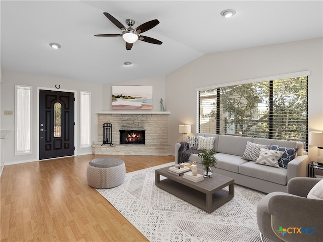 living room featuring wood-type flooring, lofted ceiling, a stone fireplace, and ceiling fan